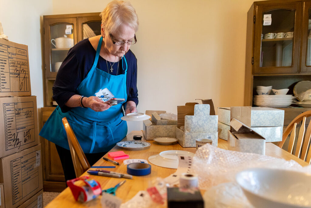 image of Elderly lady in blue nest home apron taking inventory of items to be sold at estate sale after senior move management  