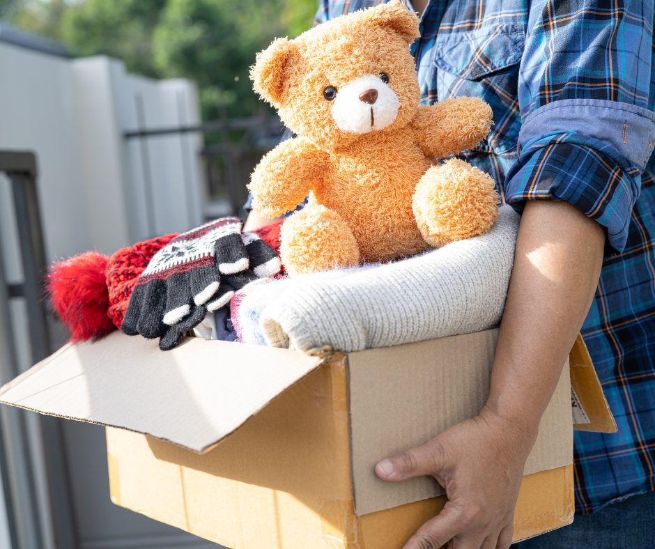 declutter a box of nice items ready to donate to a cause. Items include a teddy bear and hat and gloves. 